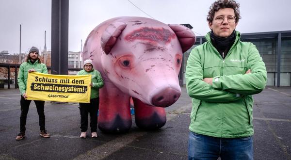 Neben einem großen aufblasbaren Schwein stehen Aktivist:innen mit einem Banner: Schluss mit dem Schweinesystem