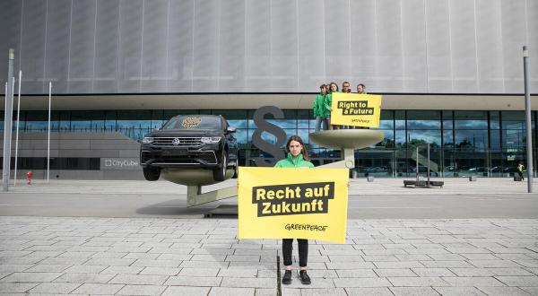 Eine überdimensionierte Waage: auf der einen Seite der schwerer wiegende VW, auf der anderen Menschen, die ein Banner halten mit der Aufschrift 2Recht auf Zukunft