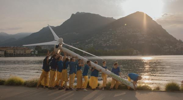In blau und gelb gekleidete Greenpeace-Aktive heben ein Windrad bei der Konferenz zum Wiederaufbau der Ukraine 2022 in Lugano