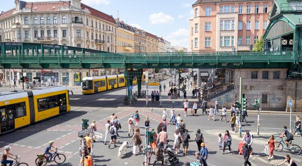 Verkehrssituation an einer Kreuzung in Berlin: zwei Straßenbahnen, eine Bahnbrücke, Radfahrende und Fußgänger:innen 