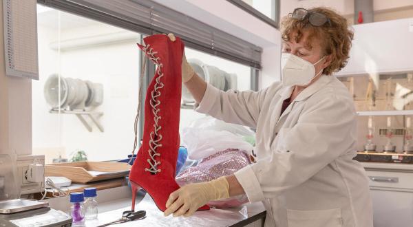 Mitarbeiterin hält im Labor einen roten High Heel-Stiefel