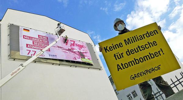 An der Fassade des Verteidigungsministeriums hängt ein 5,40 Meter mal 12,50 Meter großes Banner in der Optik eines Geldscheins. Davor ein Aktivist mit einem Banner "Keine Milliarden für Atombomber".