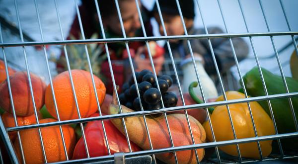 Obst und Gemüse im Einkaufswagen - im Hintergrund ein Kind und eine erwachsene Person.