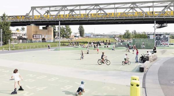 Berlin: Öffentlicher Park mit spielenden Kindern, im Hintergrund fährt eine S-Bahn über eine Brücke