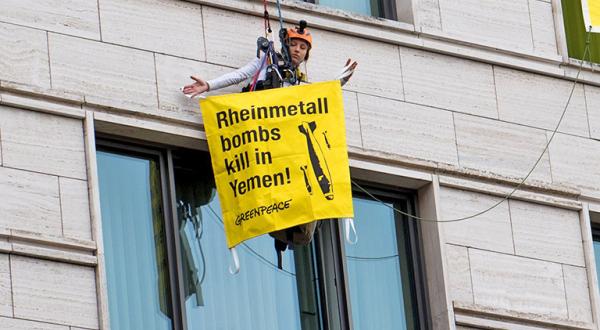Greenpeace-Kletterin an Hauswand hält Banner mit "Rheinmetalbombs kill in Jemen"