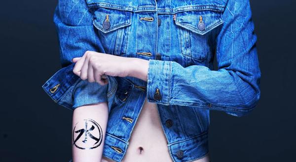 Eine Frau krempelt den Ärmel ihrer Jeansjacke hoch, darunter kommt das Detox-Logo zum Vorschein. 