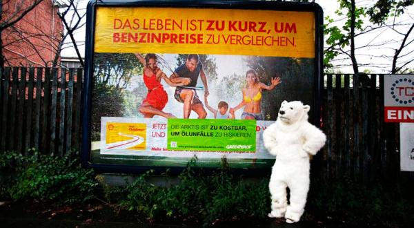 Als Eisbär verkleideter Aktivist vor beklebtem Shell-Plakat. 