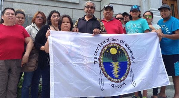 Eine Gruppe von Cree-Indianern hält ein Banner, auf dem das Logo der Waswanipi-Gemeinde zu sehen ist.  