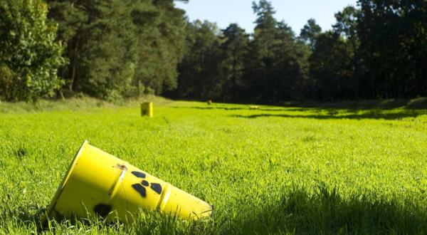 Eine Attrappe eines Atommüllfasses liegt auf einer Waldlichtung. Es wird auf die vergebliche Suche nach einem Endlager hingewiesen. 