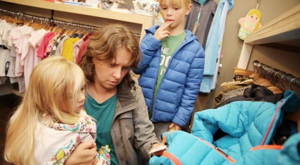 Eine Mutter mit ihren beiden Kindern beim Kauf von Kinderkleidung