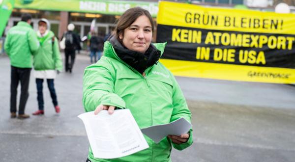 Bei einer Protestaktion verteilt eine Greenpeace-Aktivistin Info-Flyer; hinter ihr ein Banner mit der Aufschrift "Kein Atomexport in die USA".
