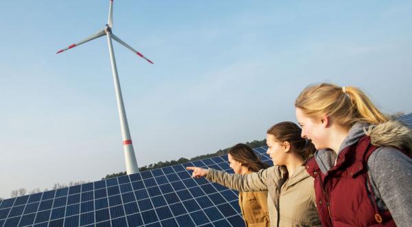 Drei junge Frauen vor Windrad und Solar-Panels in der Energie-Kommune Saerbeck