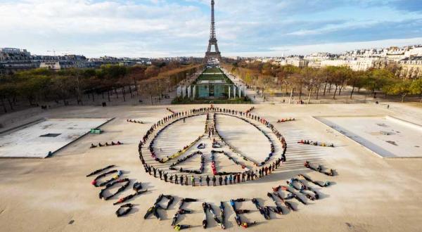 Im Pariser Park des Champ-de-Mars formen Hunderte Menschen das Eiffelturm-Friedenssymbol und darunter den Schriftzug 100% Renewable. Im Hintergrung ist der Eiffelturm zu sehen