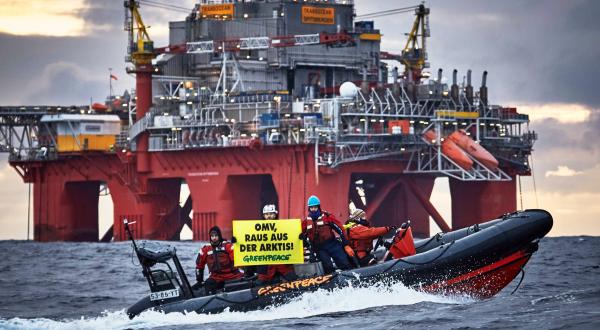 Die OMV-Ölplattform Transocean Spitsbergen; davor ein Greenpeace-Schlauchboot, auf dem Aktivisten ein Banner mit der Aufschrift "OMV, raus aus der Arktis!" in die Höhe halten