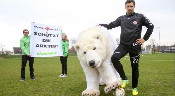 Sören Gonther, Mannschaftskapitän de FC St. Pauli, mit Eisbärdame Paula. Hinter ihnen fordern zwei Greenpeace-Aktivisten auf einem Banner: "Schützt die Arktis".