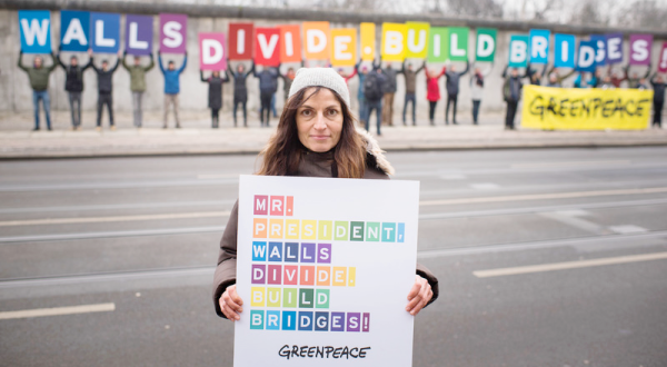 Greenpeace-Aktivisten bilden mit Buchstabentafeln die Worte "Walls devide. Build bridges" vorm Berliner Mauerdenkmal