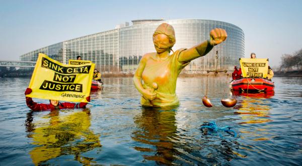 Greenpeace-Aktivisten im Schlauchboot versenken eine Statue von Justitia im Wasser, sie halten Banner "Stop Ceta"