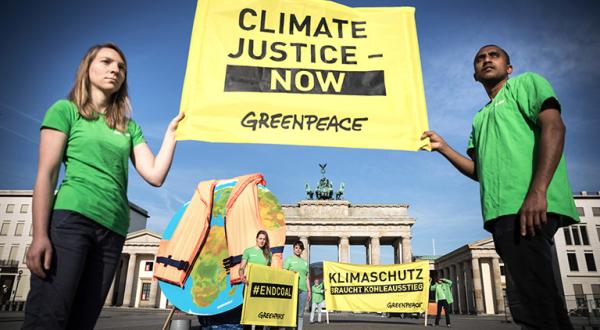 Aktivisten in Berlin vorm Brandenburger Tor, sie zeigen einen Globus mit angelegter Rettungsweste