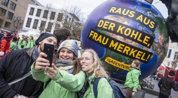 Greenpeace-Aktivisten machen ein Selfie vor Merkel-Skulptur