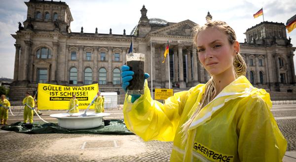 Aktivisten vor dem Reichstag in Berlin halten ein Banner mit der Aufschrift "Gülle im Wasser ist Scheiße! Politiker müssen handeln! Davor steht ein drei Meter großer mit Gülle gefüllter Suppenteller