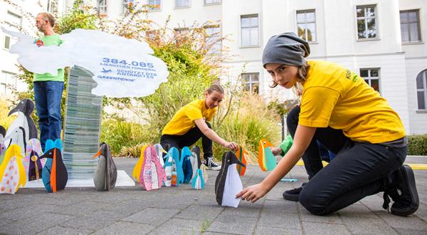 Greenpeace-Kids mit Unterschriftenstapel und Pinguinfiguren