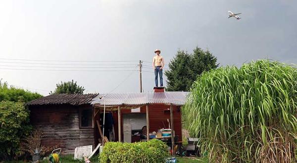 Für den Greenpeace Photo Award nominiertes Foto: Auf dem Dach eine Hütte steht ein Mann, im Vordergrund Pflanzen und Gertenwerkzeug