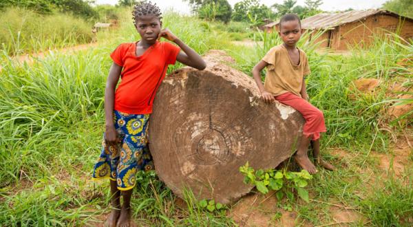 Zwei Kinder lehnen an einem geschlagenen Baumstamm