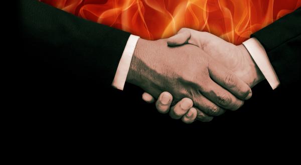 Zwei Hände reichen sich, während es im Hintergrund brennt