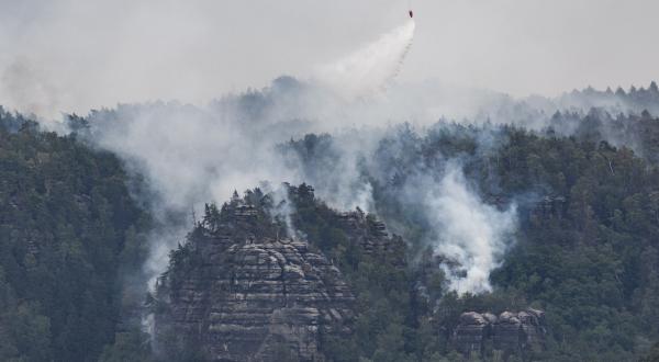 Ein Hubschrauber der Bundespolizei fliegt mit einem Löschwasser-Außenlastbehälter, um einen Waldbrand im Nationalpark Sächsische Schweiz zu löschen.