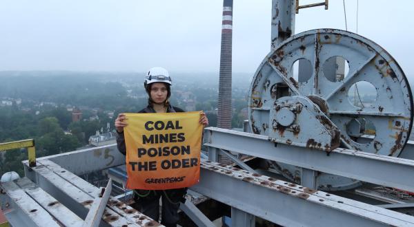 Aktivistin auf Turm in Bergbaumine, hält Banner "Coal Mines poison the Oder"