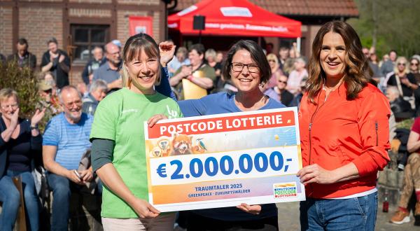 Katharina Witt überreicht zwei Personen von Greenpeace einen großen Scheck im Wert von 2.000.000 €. Im Hintergrund applaudiert eine Menschenmenge.