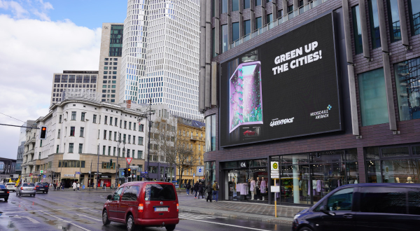 Plakat an Hochhaus hinter breiter Straße, Headline "Green up the Cities!"