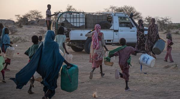 Menschen rennen mit Kanistern zu einem Hilfslaster