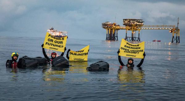 Greenpeace-Aktivisten schwimmen mit Banner und Gepäck zur Ölplattform