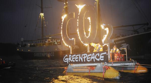 Brennendes CO2-Zeichen auf einem Greenpeace-Schlauchboot.