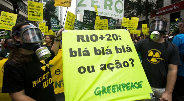 Greenpeace-Aktivisten auf der Demonstration in Rio anlässlich der Rio+20-Konferenz. Zwei Aktivisten mit Atemschutzmasken halten ein Banner mit der Aufschrift "Rio+20: blá, blá, blá ou ação? (Rio +20: bla, bla, bla oder Aktion?)