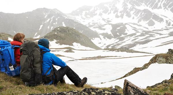 Zwei Menschen in Outdoor-Ausrüstung sitzen auf einem Felsen in den Bergen