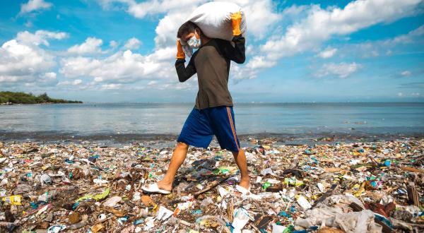Mann trägt Müllsack über völlig verdreckten Strand von Manila