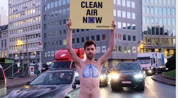 Aktivist mit nacktem Oberkörper auf dem eine blaue Lunge gemalt ist, hält ein Banner: Clean Air Now