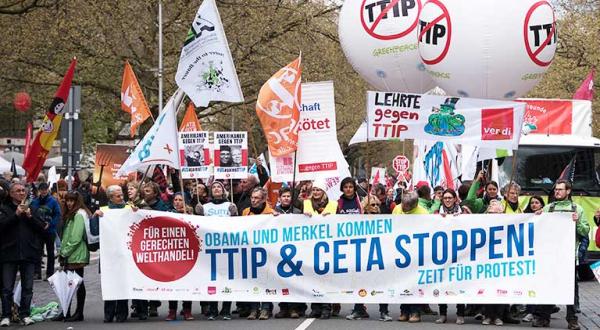 Menschen tragen auf der Demonstration in Hannover gegen TTIP und CETA ein großes Banner: Obama und Merkel kommen. CETA und TTIP stoppen! Zeit für Protest