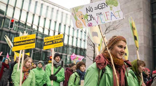 Aktivisten fordern auf der "Wir haben es satt!"-Demo "Stoppt Tierfabriken, TTIP und Gentechnik". Sie tragen Schilder mit der Aufschrift "TTIP = Gentechnik".