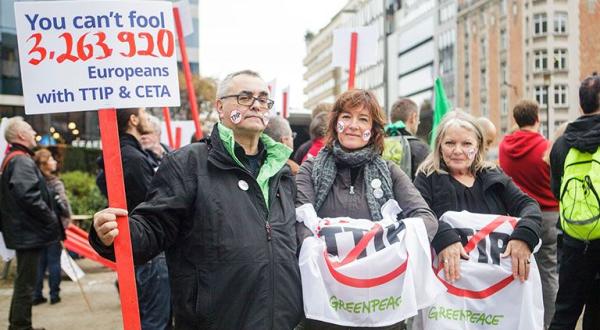 Ein Mann und zwei Frauen von Greenpeace stehen in Brüssel vor der Europäischen Kommission. Der Herr hält ein Schild in der Hand mit der Aufschrift: „You can’t fool 3.263.920 Europeans with TTIP & CETA“.