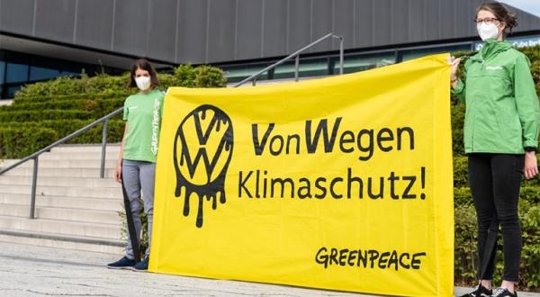Zwei Aktivist:innen halten ein Banner "Von Wegen Klimaschutz" vor der VW-Hauptversammlung in Berlin.