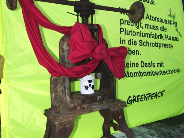 Greenpeace-Aktivist:innen bauen eine Schrottpresse vor dem Siemens Plutoniumwerk auf. Auf dem Transparent: "Weihnachtswunsch 2003: Wer den Atomausstieg predigt, muss das Plutoniumwerk Hanau zur Schrottpresse geben. Keine Geschäfte mit Atombombentechnologie."