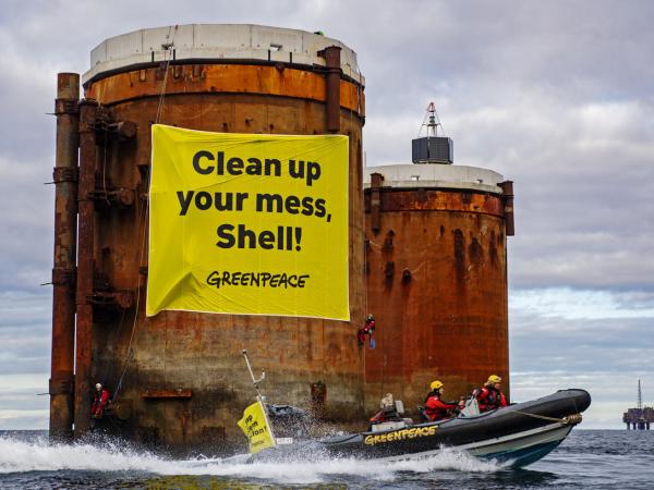 Kletterer:innen erklimmen Ölplatformen  und hängen Banner mit der Aufschrift "Shell, räumt euren Dreck weg" und "Stoppt die Meeresverschmutzung" auf.