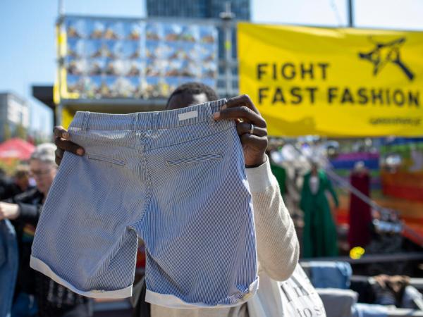 Ein Mann hält auf einer Kleidertauschparty eine Hose hoch, im Hintergrund ein Banner: "Fight Fast Fashion"