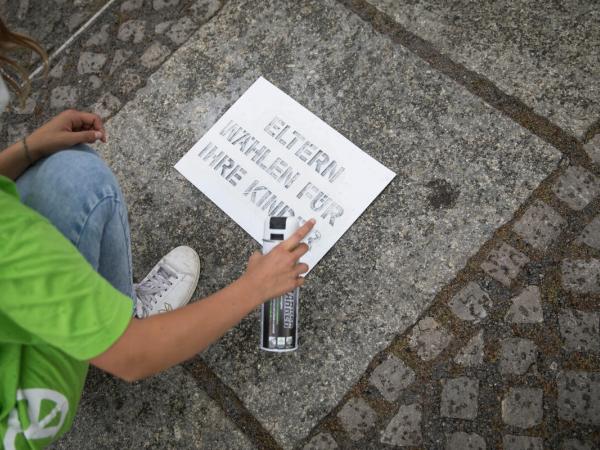 Junge Greenpeace-Aktivist:innen demonstrieren für Klimaabstimmung in Berlin. Mit Sprühkreide schreiben sie "Eltern wählen für ihre Kinder" auf den Boden. Mit einem 6 x 30 m großen Schriftzug aus einzelnen Stoffbuchstaben platzieren sie die Worte "Klima" "#vote 4 me" und ein überdimensionales Wahlkreuz auf dem Reichstagsrasen.