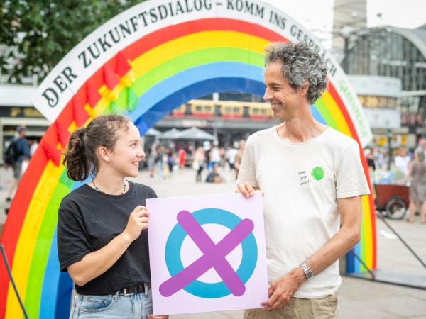 Mädchen und Mann mit vote4me Logo vor Regenbogen aus bunten Zetteln