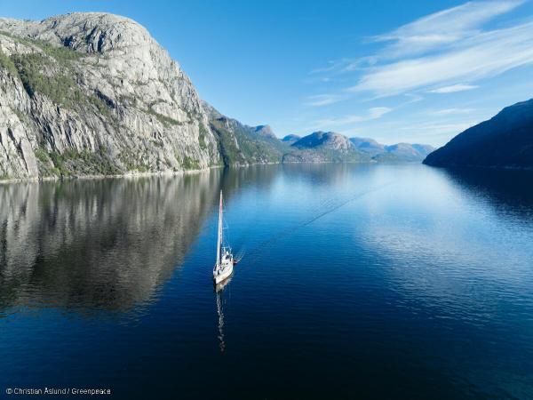 Ein Segelboot segelt durch einen Fjord mit Bergen im Hintergrund und klarem blauen Wasser.
