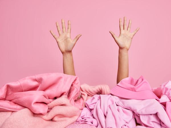 Nach oben gereckte Arme hinter einem rosa Kleiderhaufen